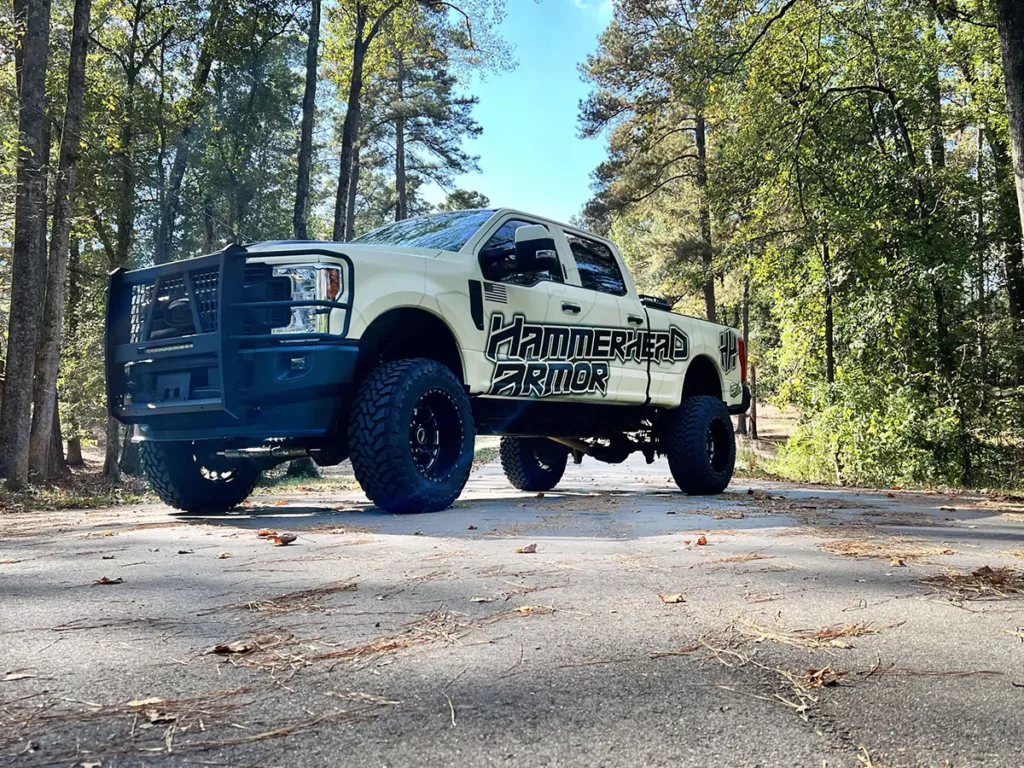 A pickup truck equipped with a HammerHead Armor Defender Series bumper, with a forest in the background.