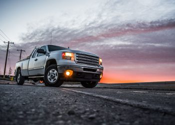 White Truck with headlights on on an empty highway with a pink and purple sunset skyline