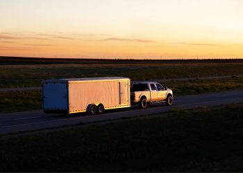 pick-up truck towing a large trailer with a rear mounted trailer hitch on an open highway at sunset