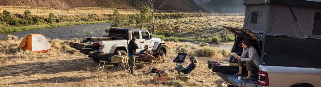 A group of people sit at a campsite in a dry field, next to a truck with Decked truck bed drawers.