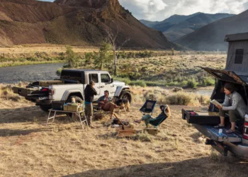 A group of people sit at a campsite in a dry field, next to a truck with Decked truck bed drawers.