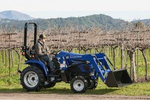 A winery worker maneuvering a Solectrac e25 electric tractor through a Vineyard