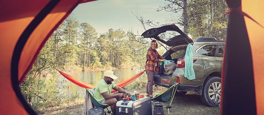 couple camping near river setting up campsite with Dometic electric cooler full of food and beverages