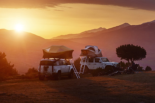 Two Thule Approach Rooftop Tents installed on top of off-road vehicles and set up at mountainous campsite
