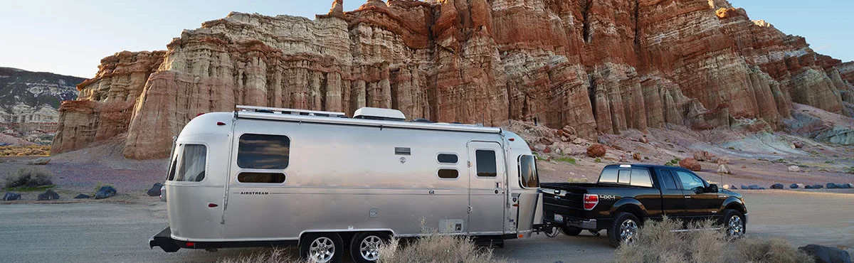 A black pickup truck hauls a travel trailer offroad through the desert.